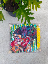 Load image into Gallery viewer, A vibrant, multicolored abstract painting on raw canvas, featuring palette knife strokes, placed on a concrete surface with a potted plant in the background.
